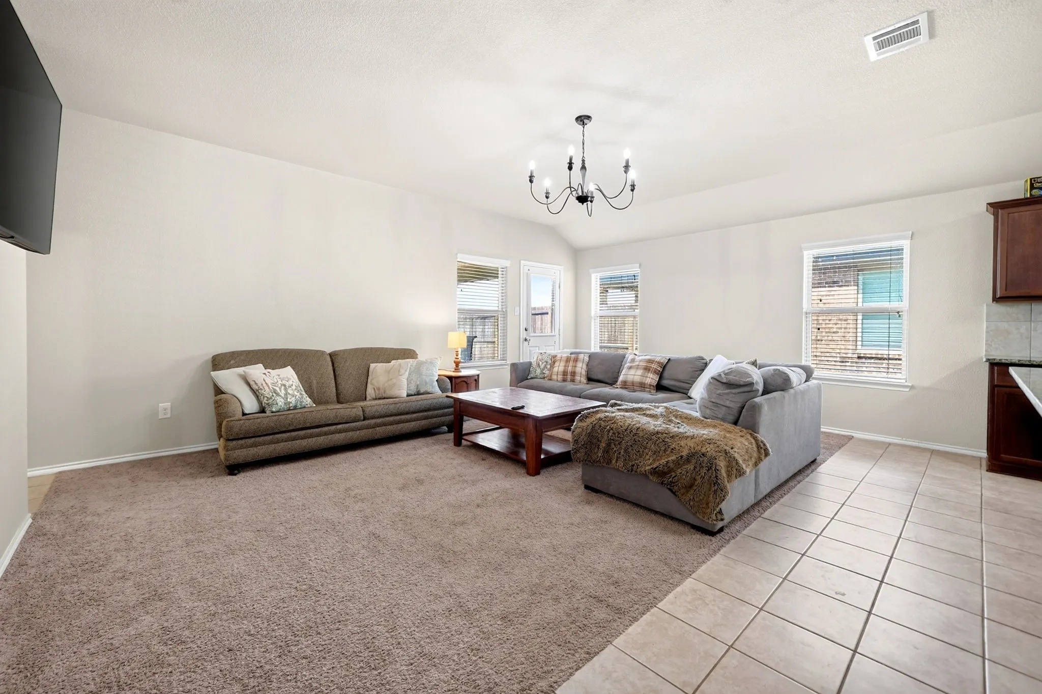 Spacious living area featuring neutral-toned walls, high vaulted ceilings, a prominent chandelier, and a combination of carpet and tile flooring