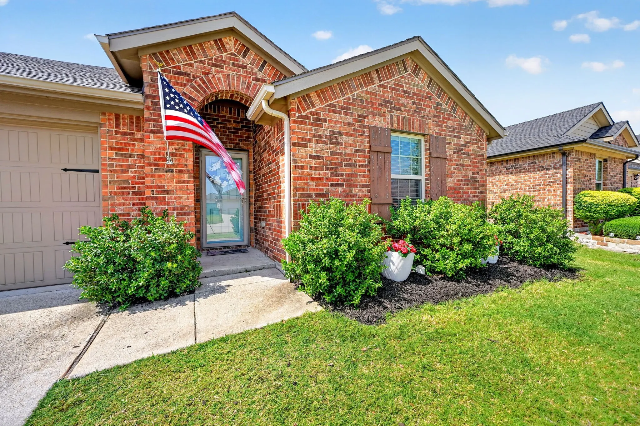 Brick exterior with arched entryway, wood-finish garage door, and decorative window shutters