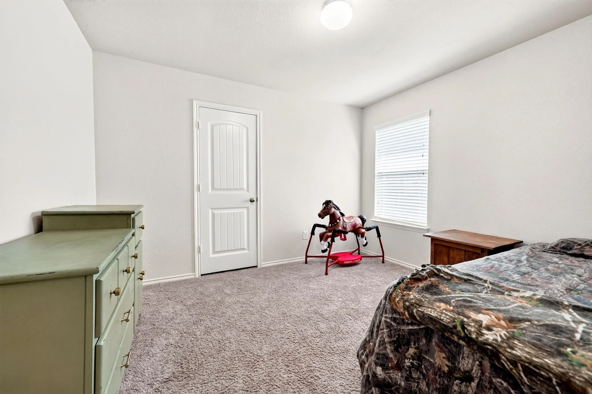 Neutral wall finishes, textured carpeting, a single window with blinds, and a white interior door with paneling