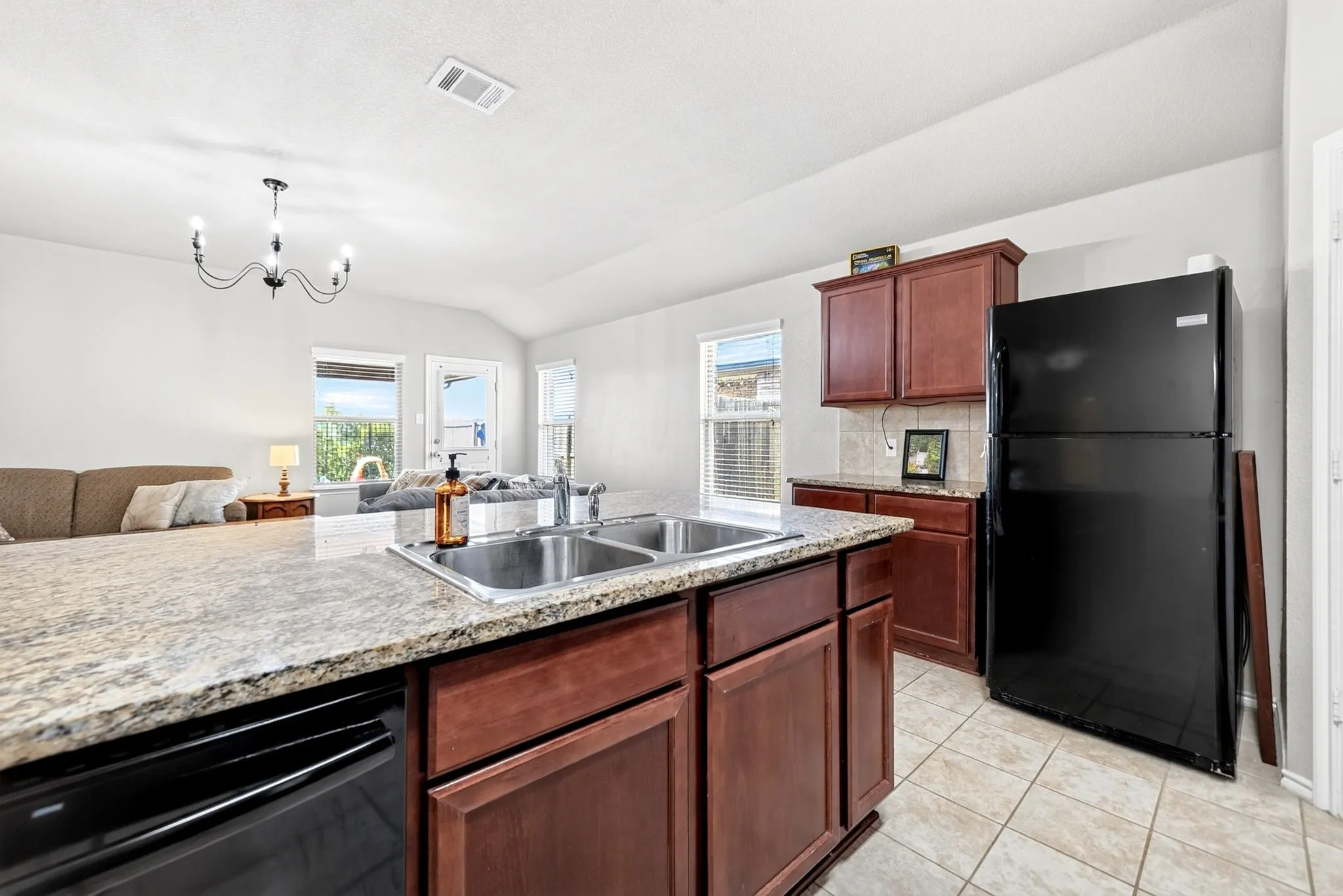 Kitchen featuring a double basin stainless steel sink, granite-style countertops, wood-finish cabinetry, and tile flooring