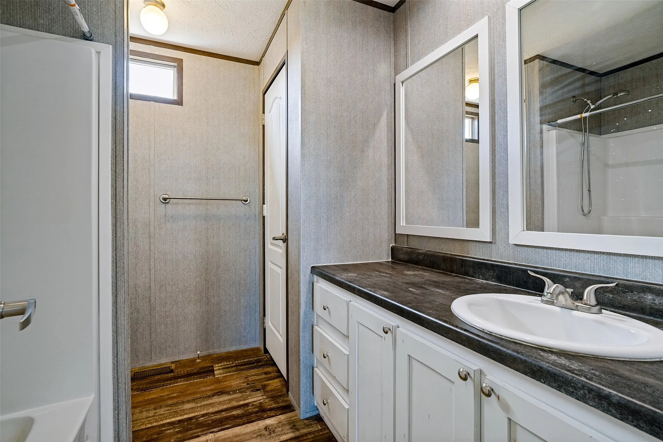 Wood-finish flooring, white vanity with cabinet storage, countertop with integrated sink, framed mirrors, and a built-in shower