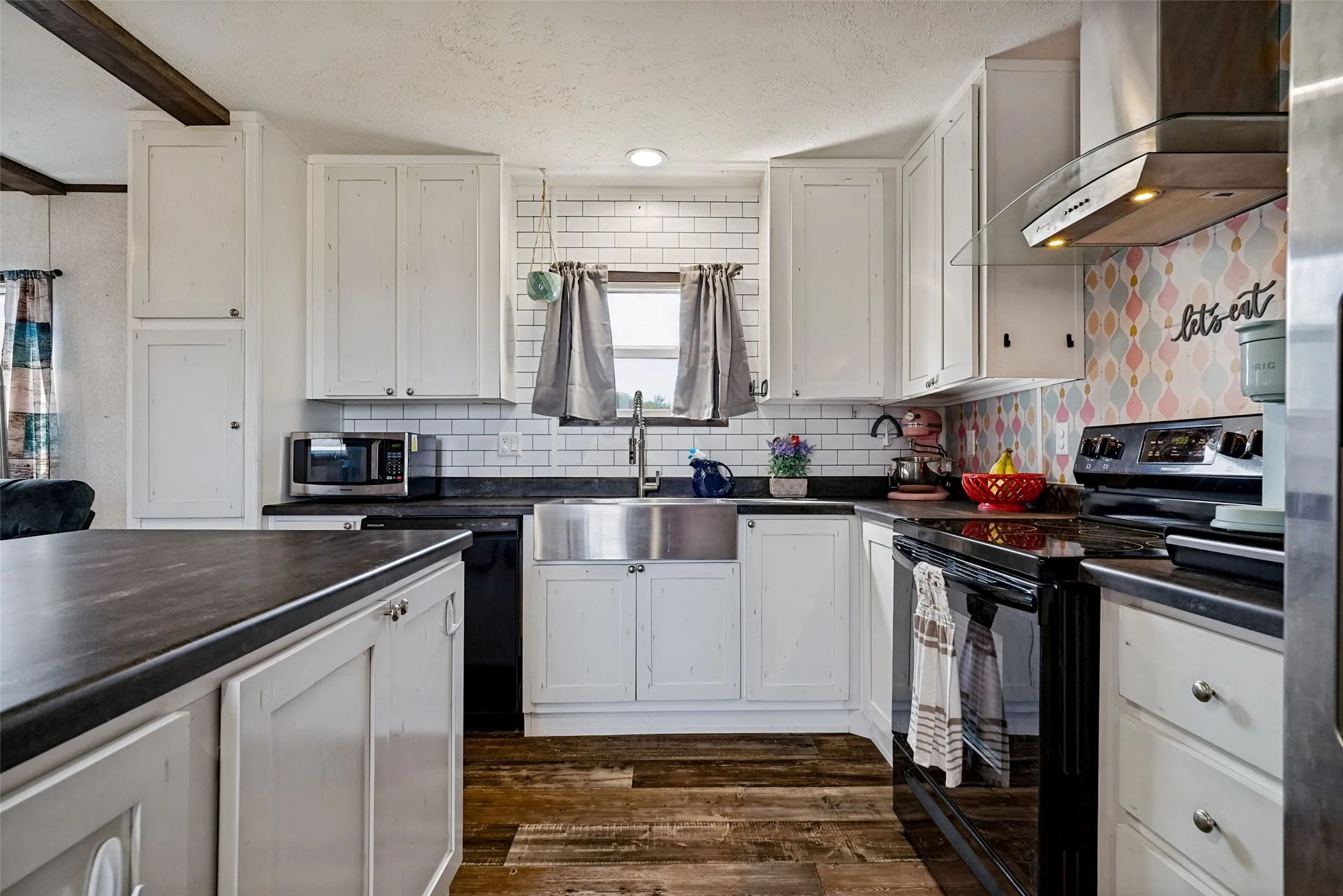 Kitchen featuring white cabinetry, dark countertops, a subway tile backsplash, a stainless steel apron sink, and wood-finish flooring