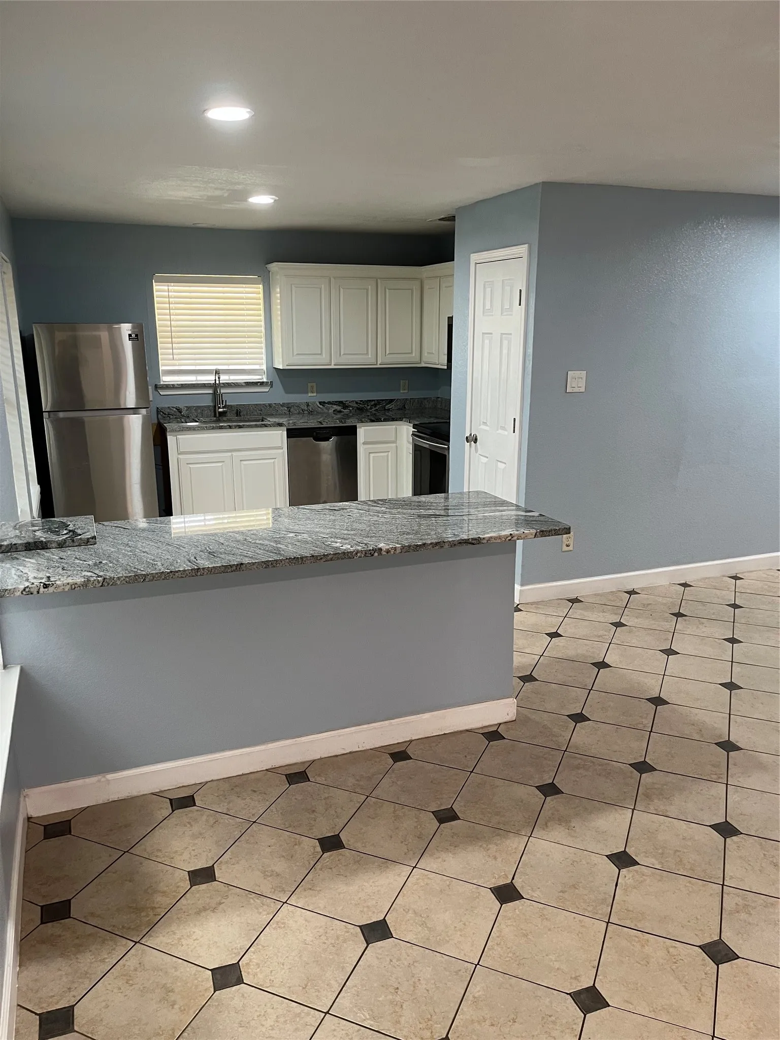 Kitchen with dishwasher, light tile floors, stone countertops, white cabinetry, and refrigerator