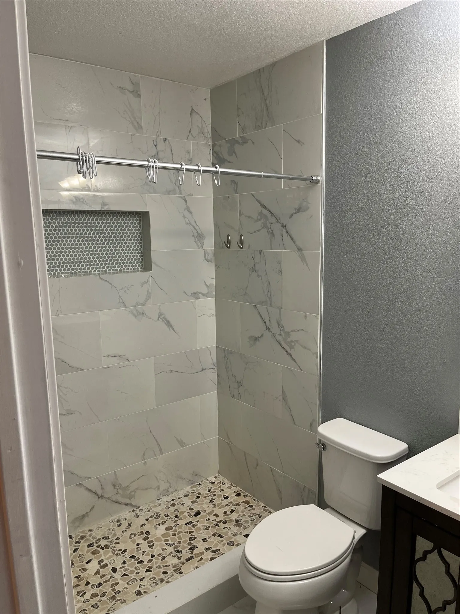 Main bathroom featuring a tile shower, a textured ceiling, toilet, and vanity.