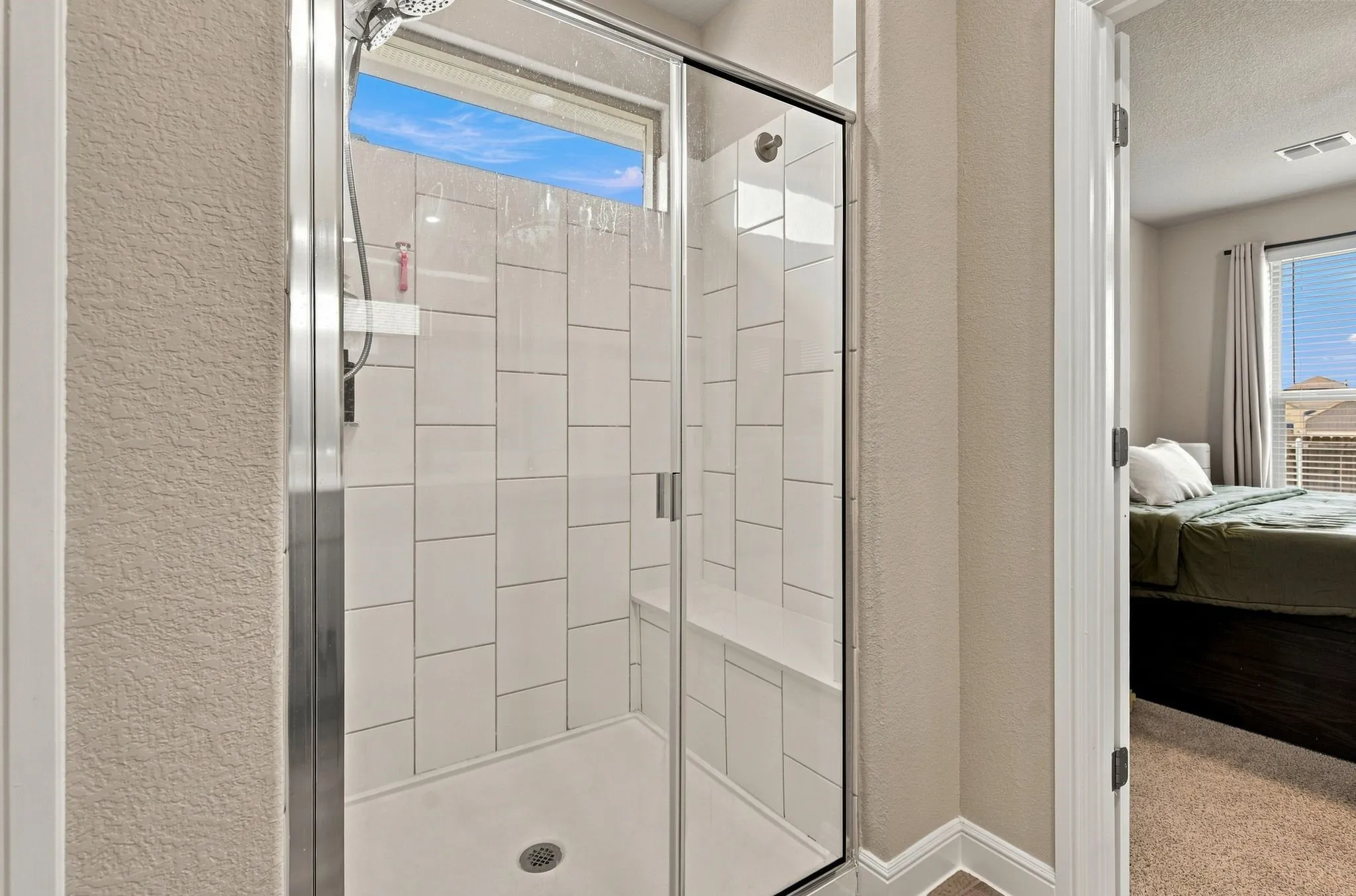 Glass-enclosed shower with subway tile surround, built-in bench, and a transom window