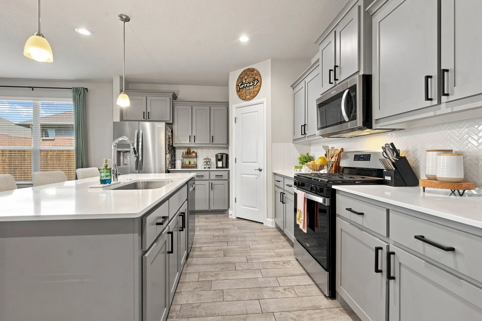 Kitchen featuring gray cabinetry, stainless steel appliances, a large island with an integrated sink, white countertops, and wood-finish flooring