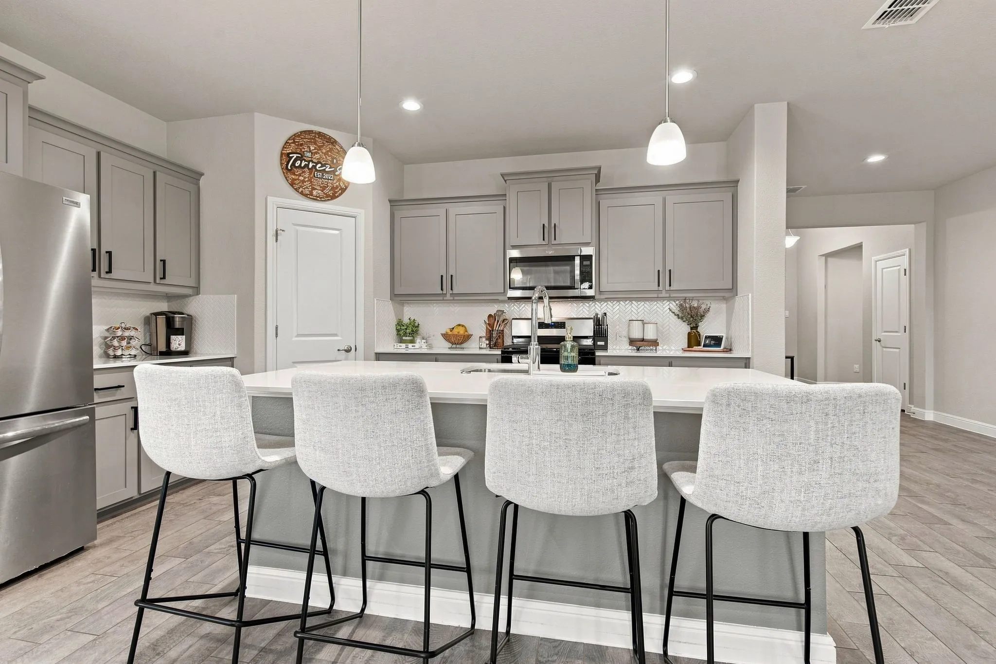 Kitchen featuring a substantial island with seating, stainless steel appliances, grey cabinetry, and wood-finish flooring
