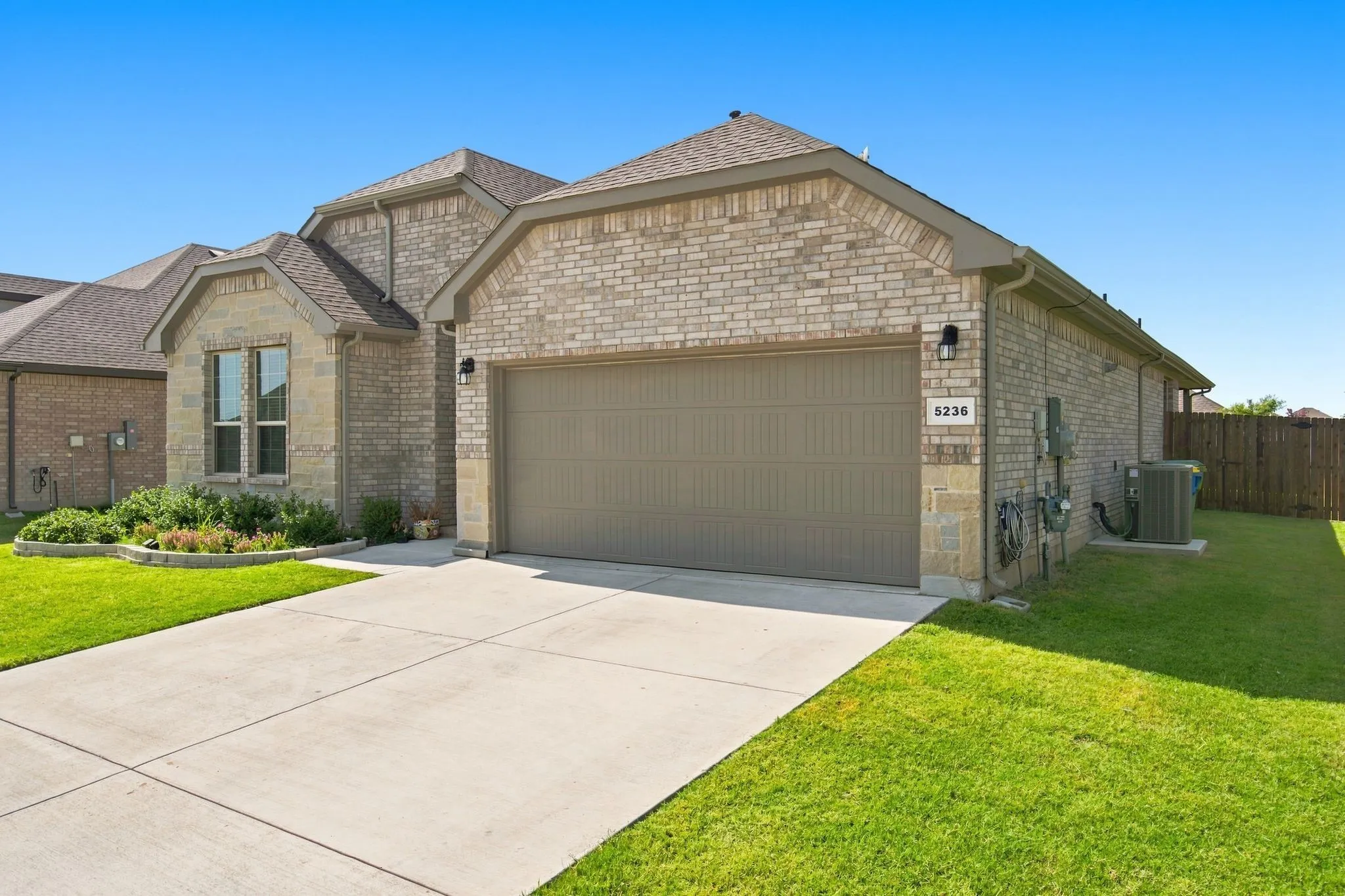 Brick exterior with stone accents, attached garage, concrete driveway, and landscaped front garden