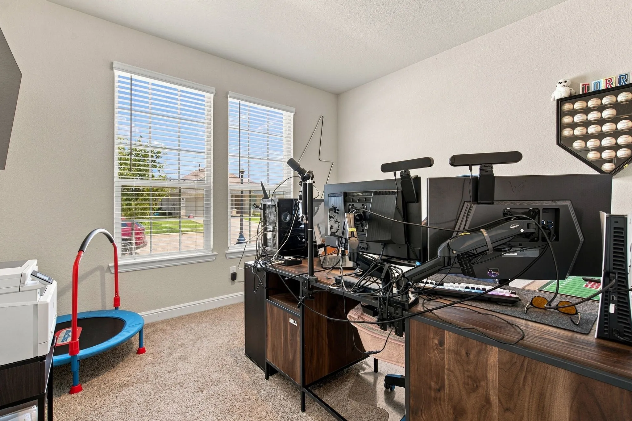 Carpeted room with two windows featuring blinds, neutral wall paint, and a wood-finish desk