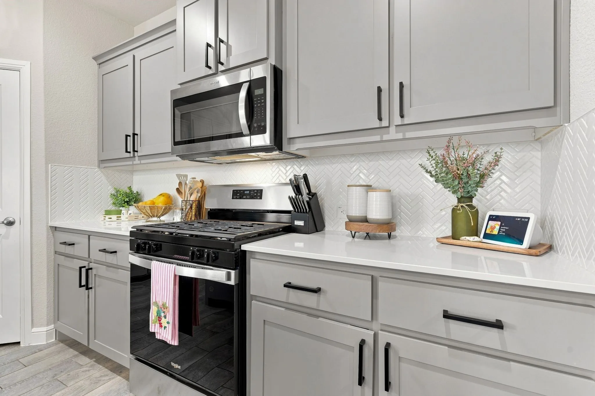 Gray shaker-style cabinetry with black hardware, white countertops, herringbone tile backsplash, stainless steel microwave, and a black gas range