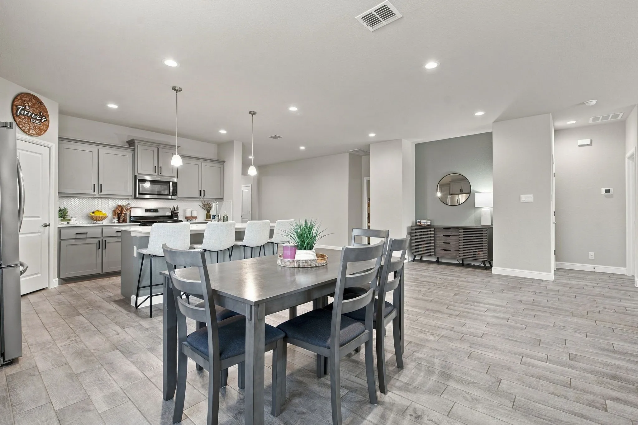 Open-concept living space featuring wood-finish flooring, recessed lighting, and a kitchen with light gray cabinetry, a white tile backsplash, and a central island