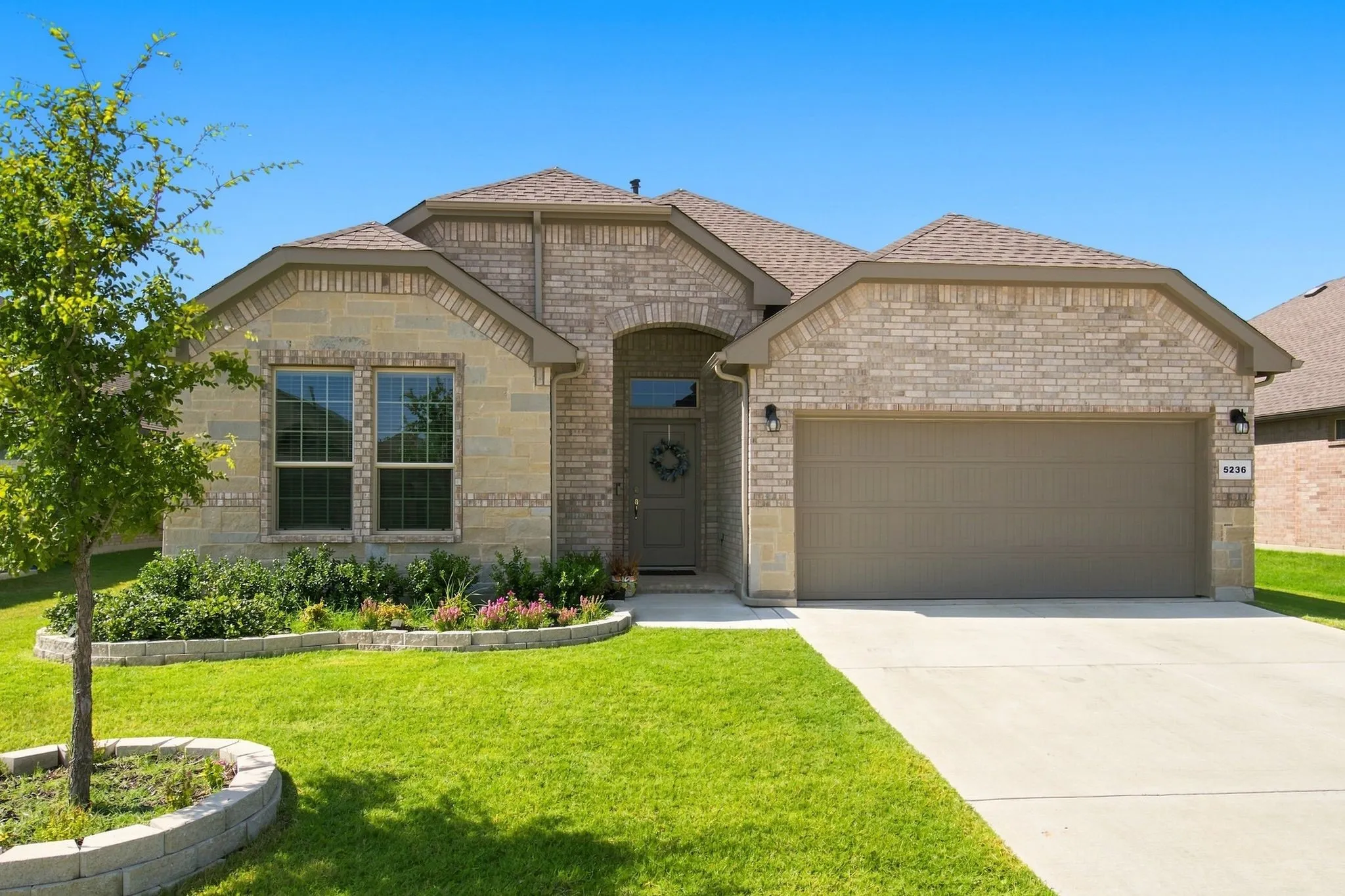 Brick and stone exterior with an arched entryway, attached garage, and a concrete driveway