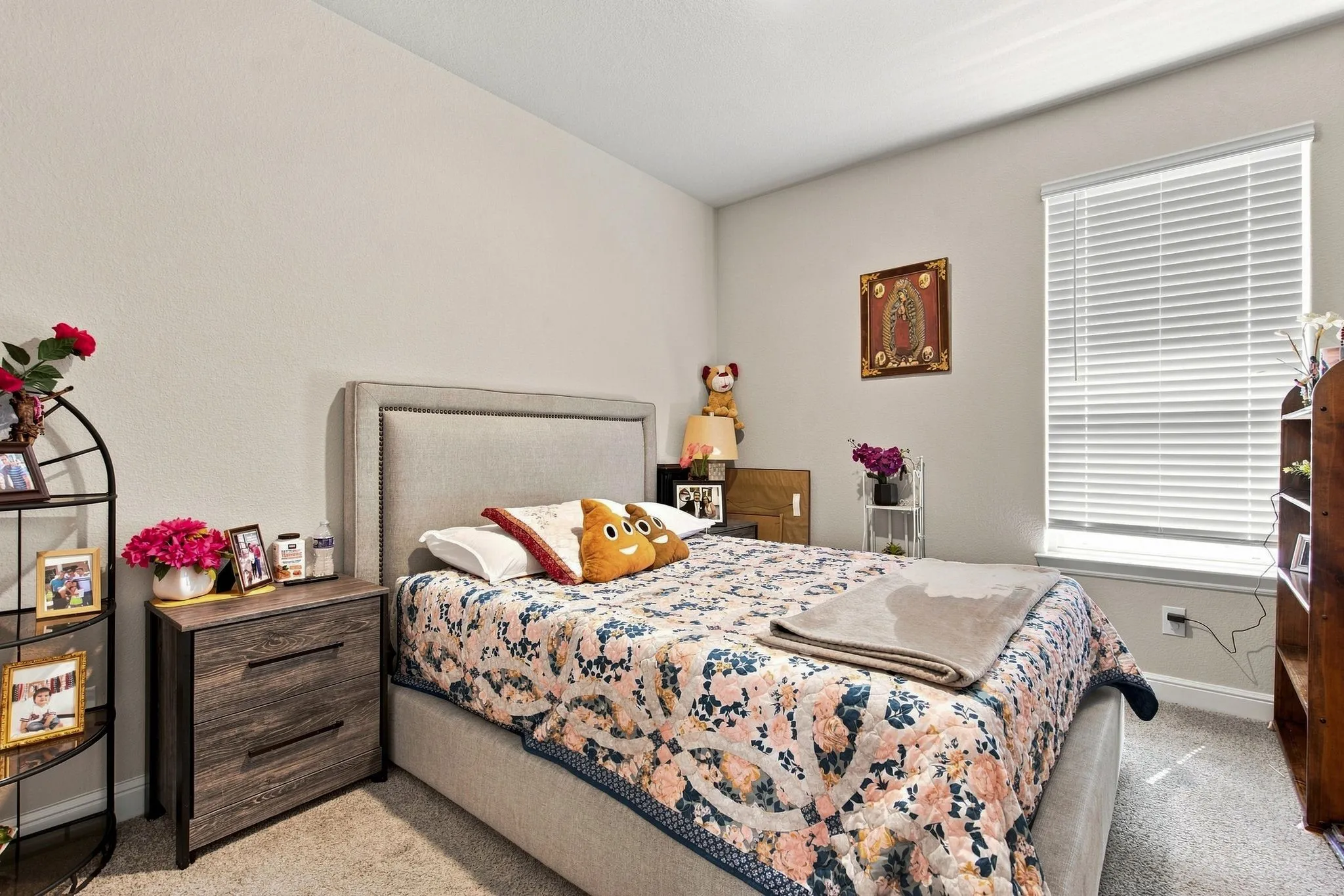 Textured wall finish, upholstered headboard, wood-finish nightstand with drawers, window with blinds, and carpeting