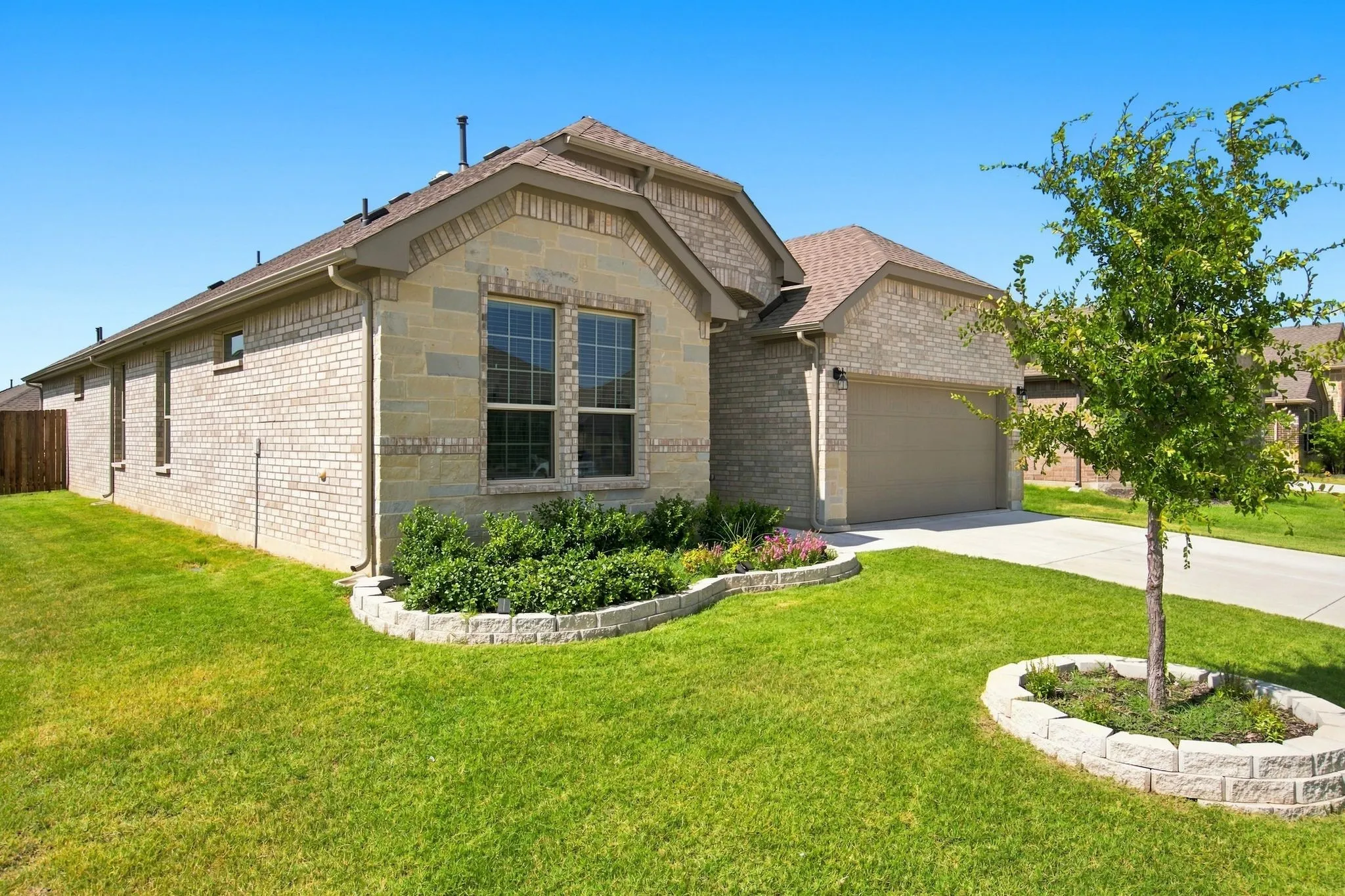 Brick and stone exterior featuring a two-car garage, front yard landscaping with stone-edged flower beds, and a paved driveway