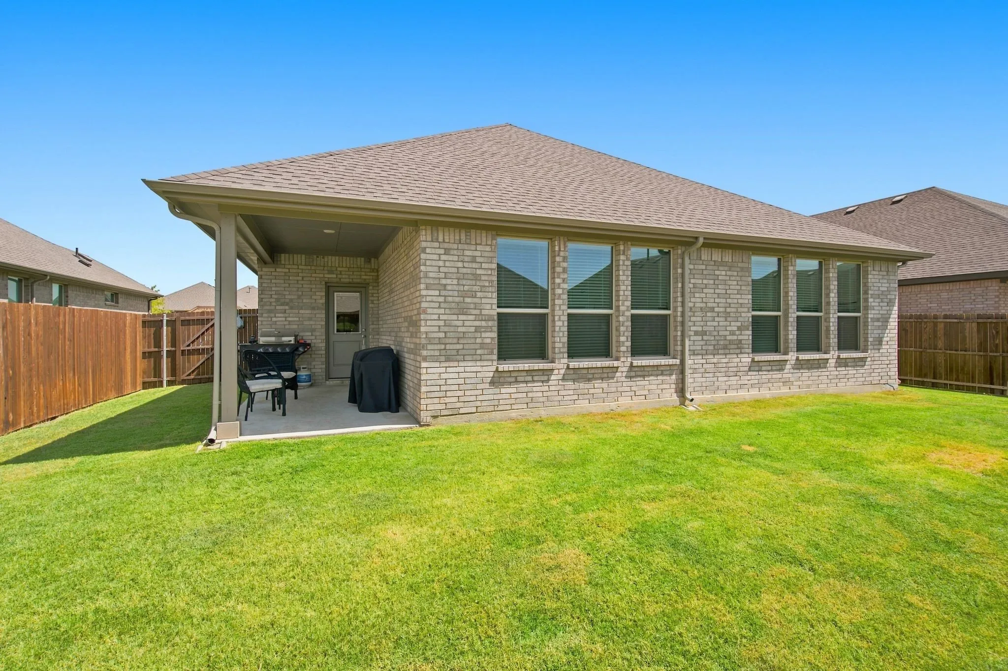 Brick exterior with multiple rear windows, covered patio, and wood-fencing