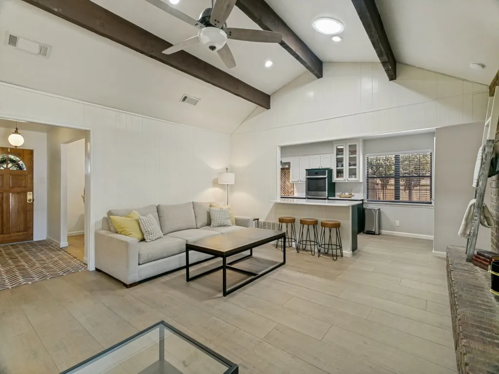 The spacious living room features a vaulted ceiling with decorative beams and an eye-catching brick fireplace.