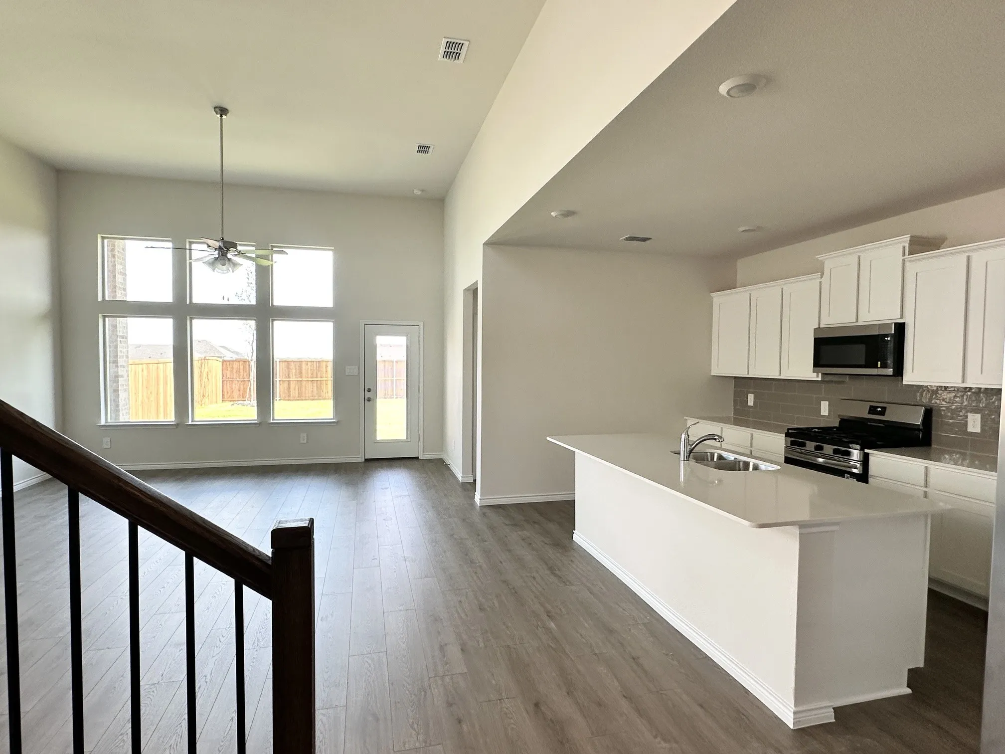 High ceilings, wood-finish flooring, white kitchen cabinetry, kitchen island with integrated sink, and stainless steel appliances