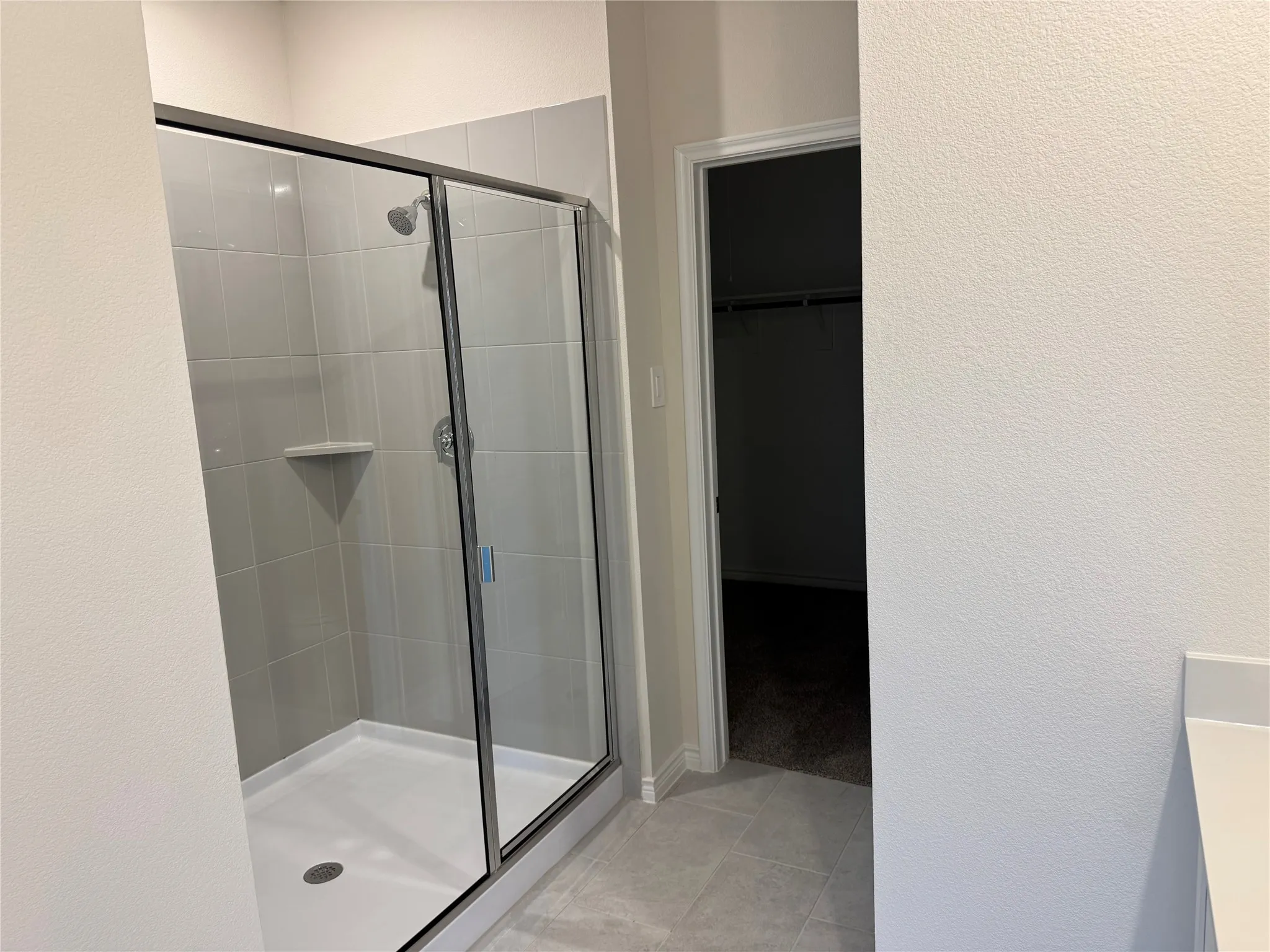 Glass-enclosed shower with a chrome shower head and built-in corner shelf