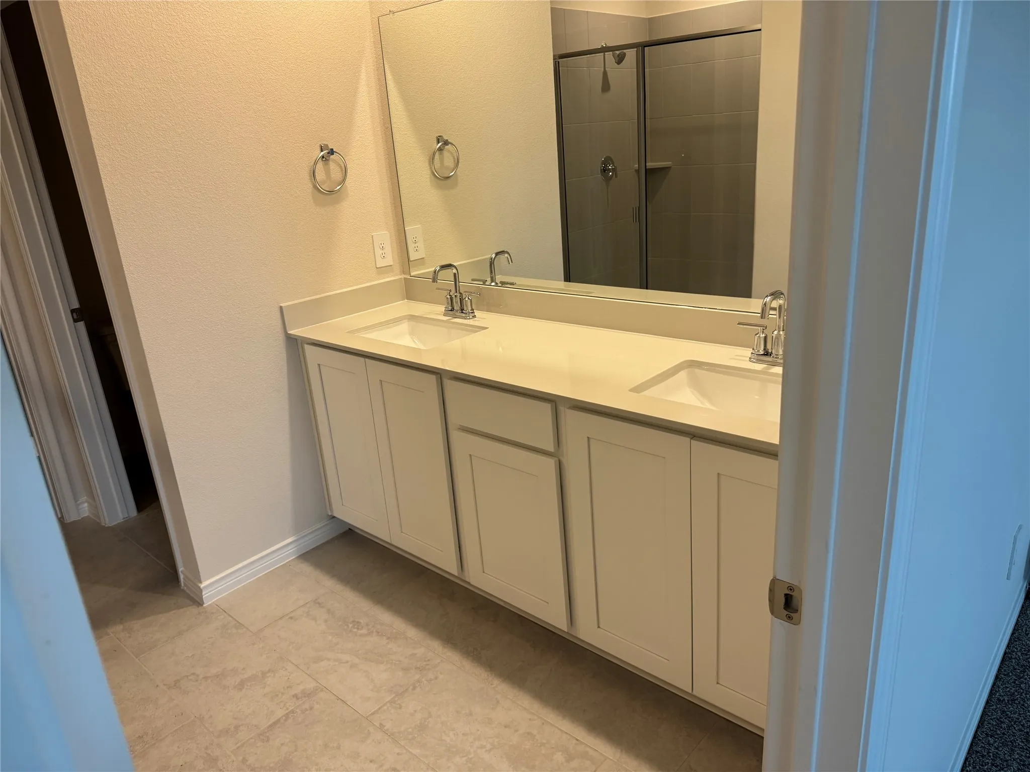 Dual vanity with integrated sinks, polished chrome fixtures, expansive mirror, and tile flooring