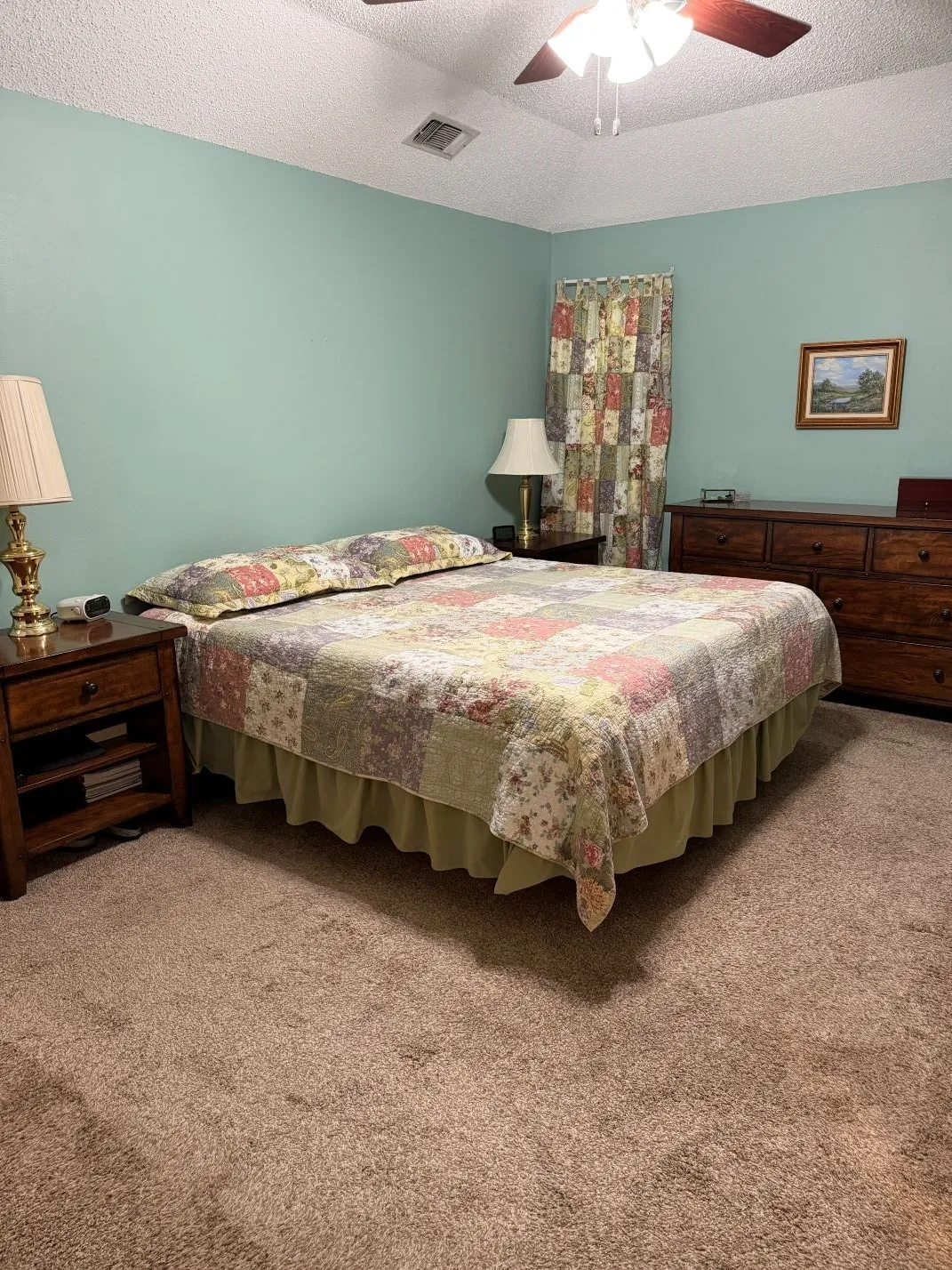 Spacious bedroom featuring soft turquoise walls, carpeted flooring, and wood-finish bedroom furniture