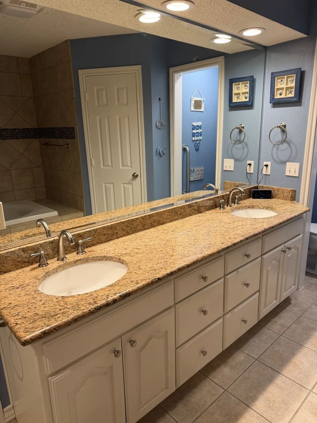 Spa-inspired master bathroom featuring dual vanities with ample storage, warm-toned natural stone countertops, and polished chrome fixtures