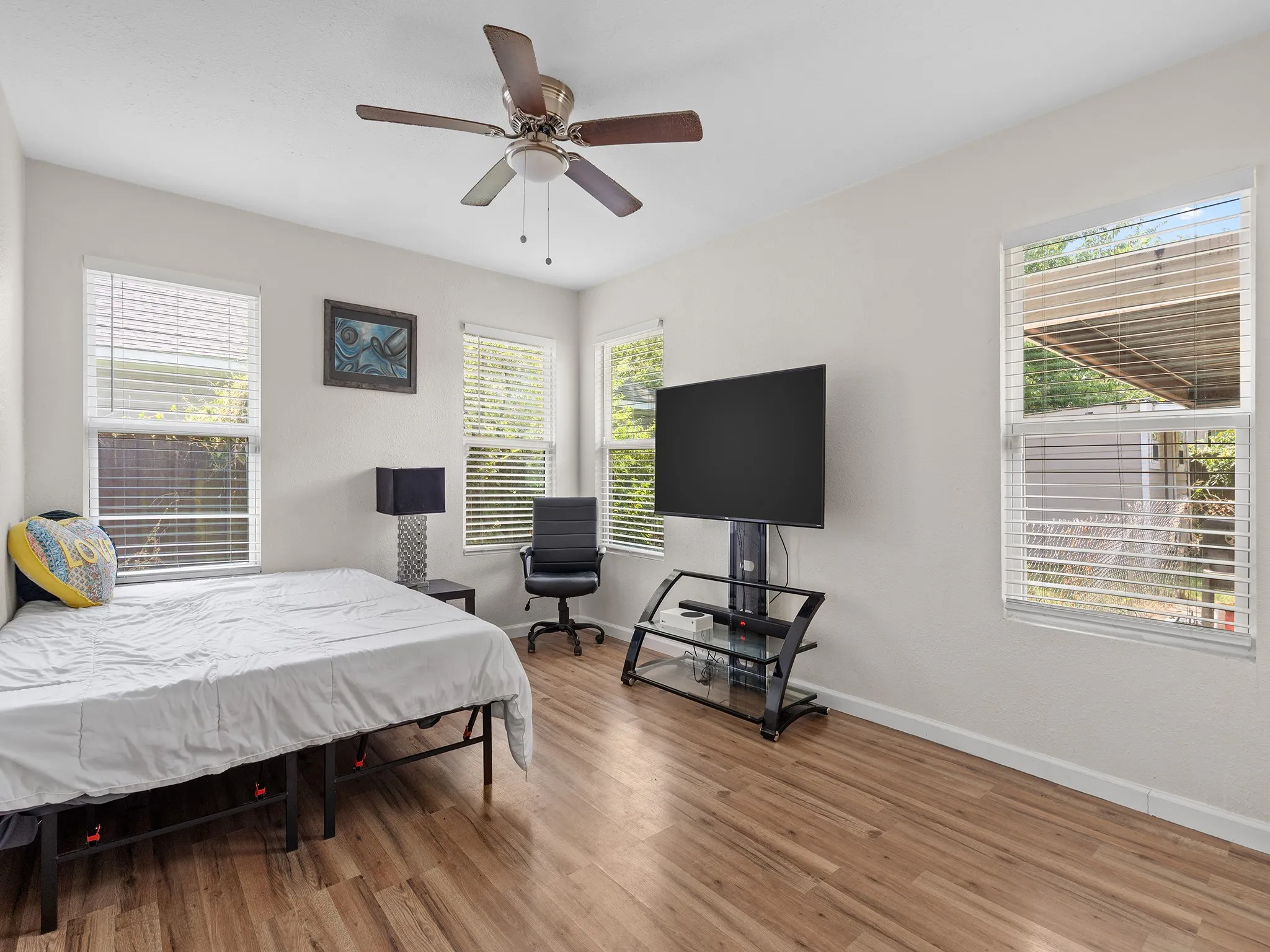 Bright bedroom with multiple windows bringing in abundant natural light, smooth vinyl flooring, neutral finishes and a ceiling fan.