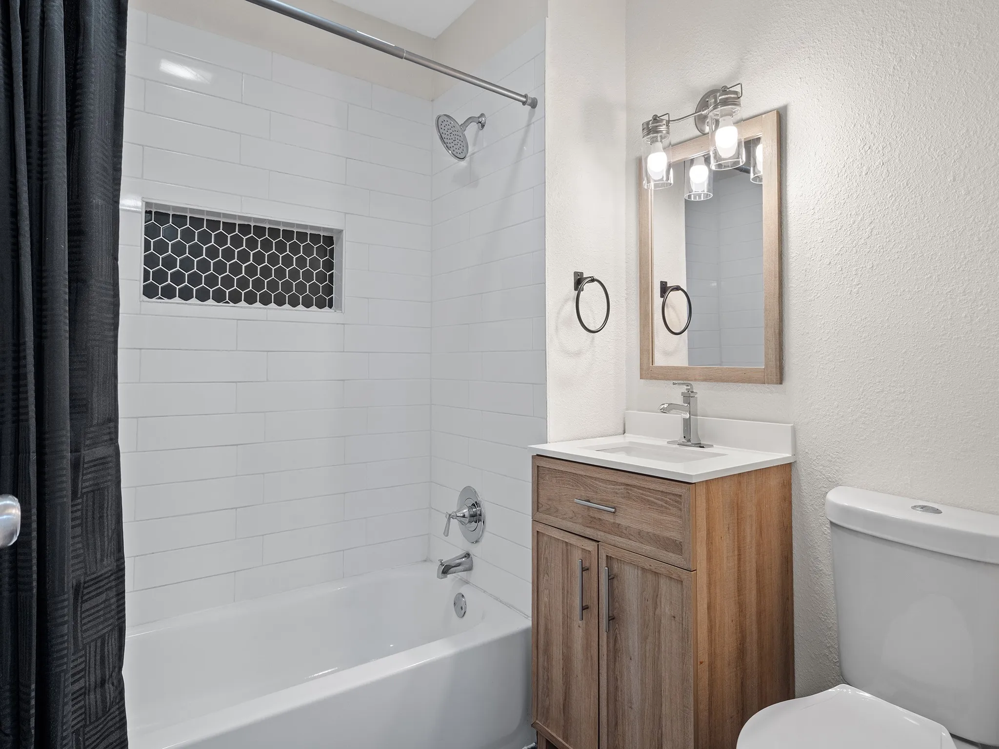 White subway tile shower surround with a hexagonal tile niche with matching hexagonal tile flooring.