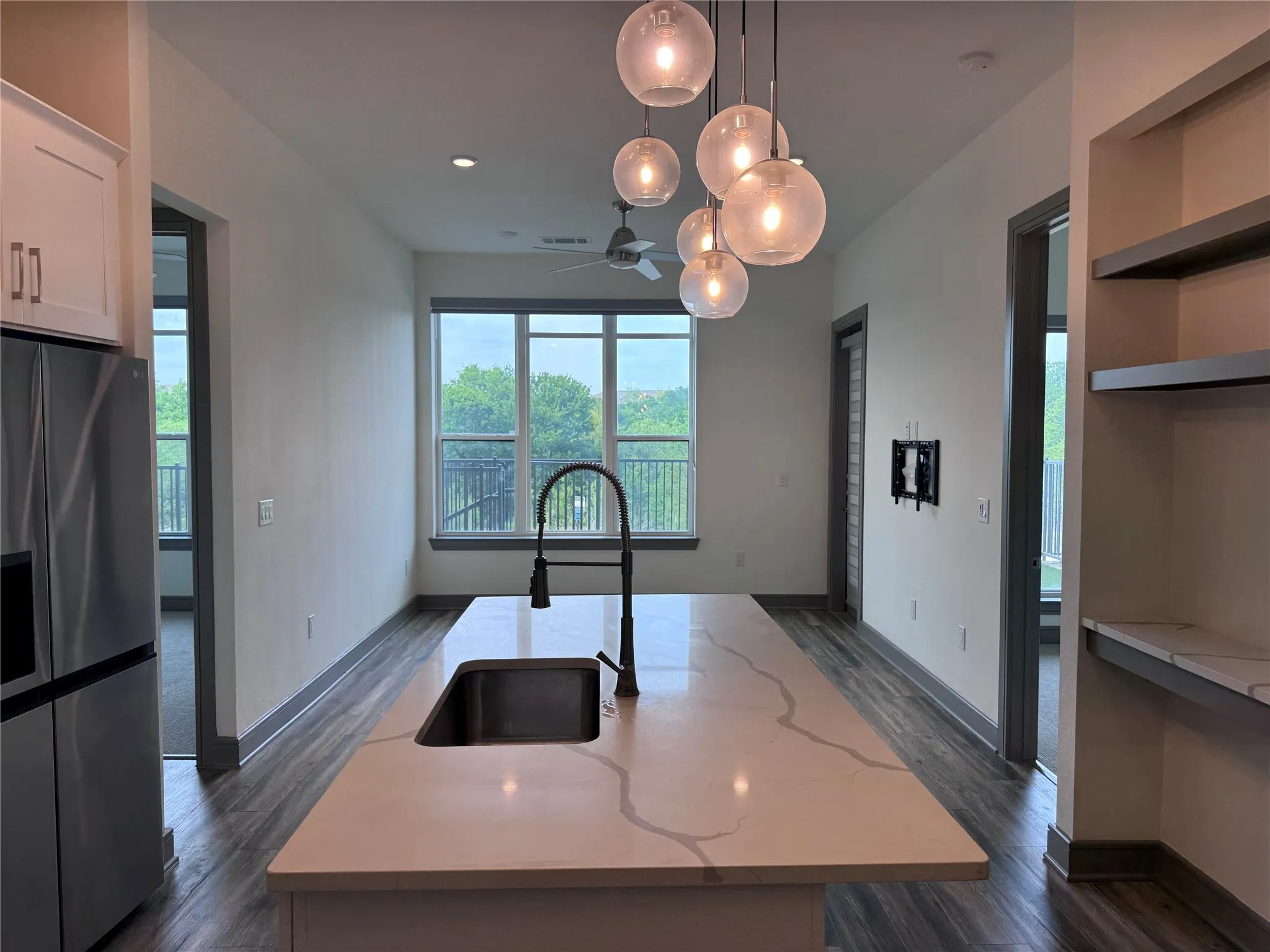 Kitchen island with integrated sink, contemporary pendant lighting, wood-finish flooring, built-in shelving, and stainless steel refrigerator