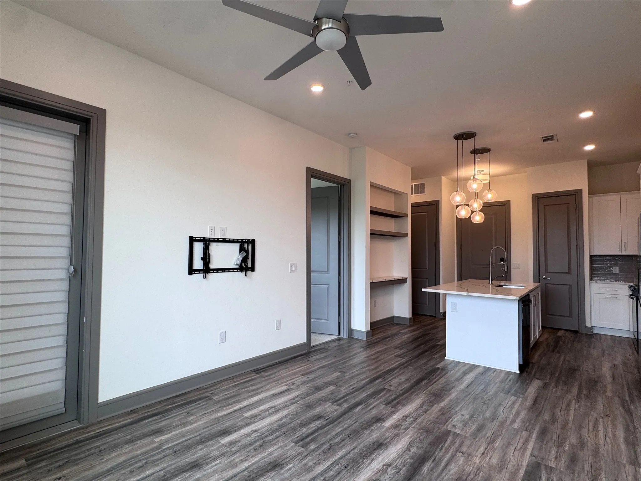 Wood-finish flooring, ceiling fan, contemporary pendant lighting, kitchen island with integrated sink, and built-in shelving with desk