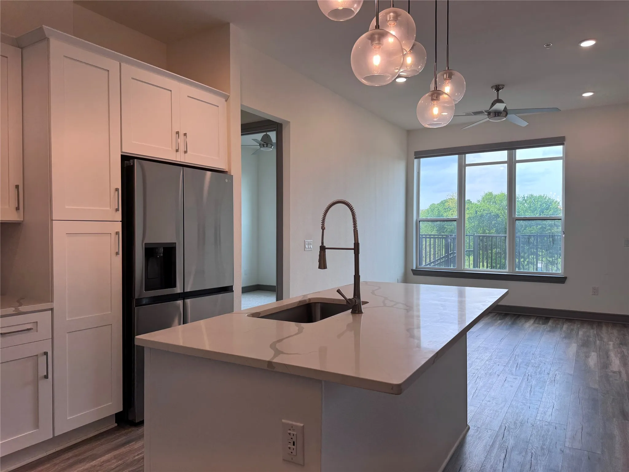 Kitchen island with integrated sink, white cabinetry, stainless steel refrigerator, contemporary pendant lighting, and wood-finish flooring