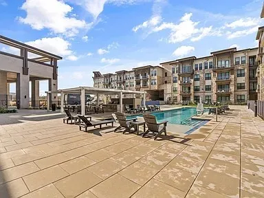 Expansive outdoor patio with a swimming pool, covered lounge area, and adjacent multi-story residential building with private balconies