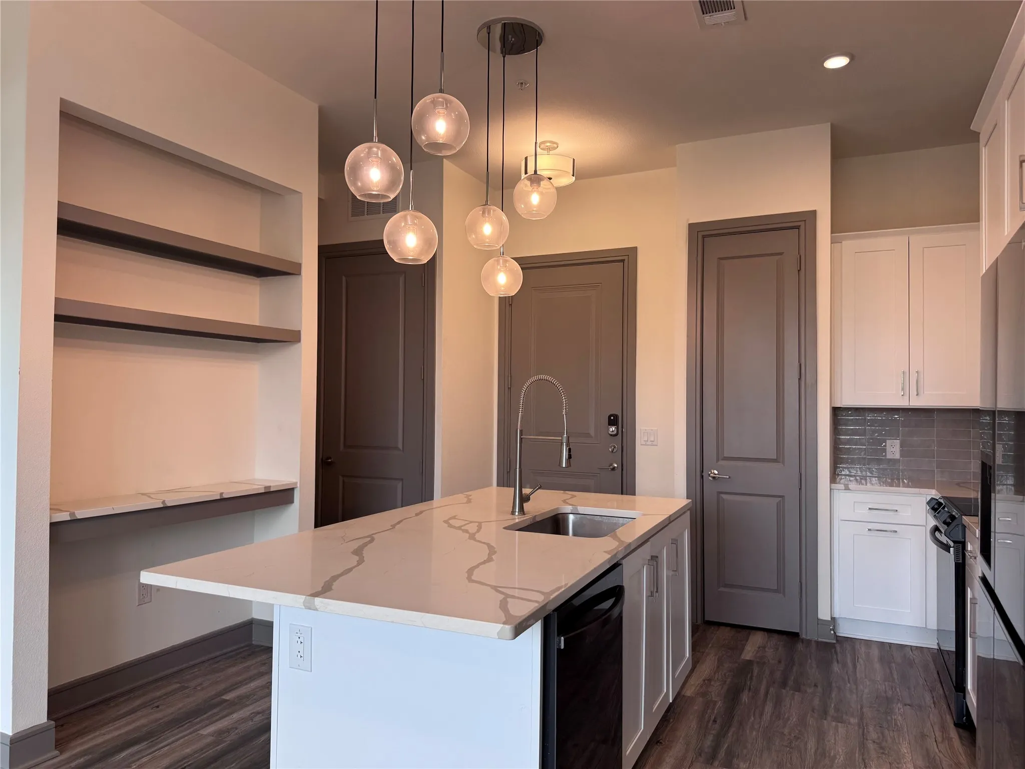Kitchen featuring a quartz-top island with integrated sink, wood-finish flooring, white cabinetry, built-in shelving, and pendant lighting