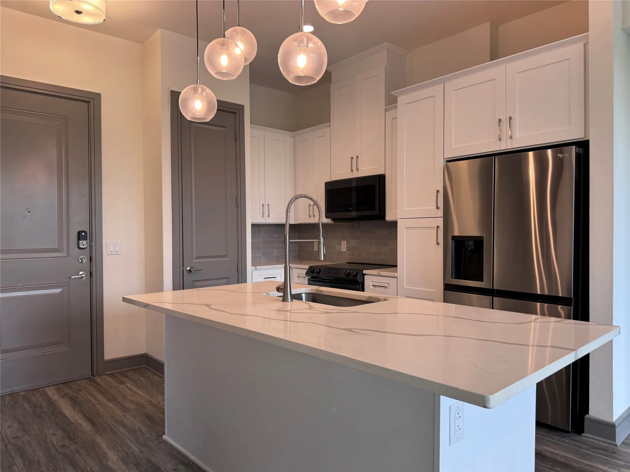Modern kitchen featuring white cabinetry with brushed nickel hardware, quartz countertop with waterfall island edge, stainless steel appliances including a built-in wall oven, and pendant lighting with frosted glass shades