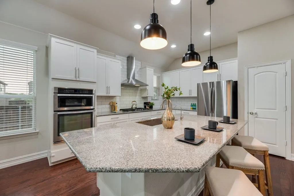 Modern kitchen featuring white shaker cabinetry, stainless steel appliances, a large island with a composite countertop, and wood-finish flooring