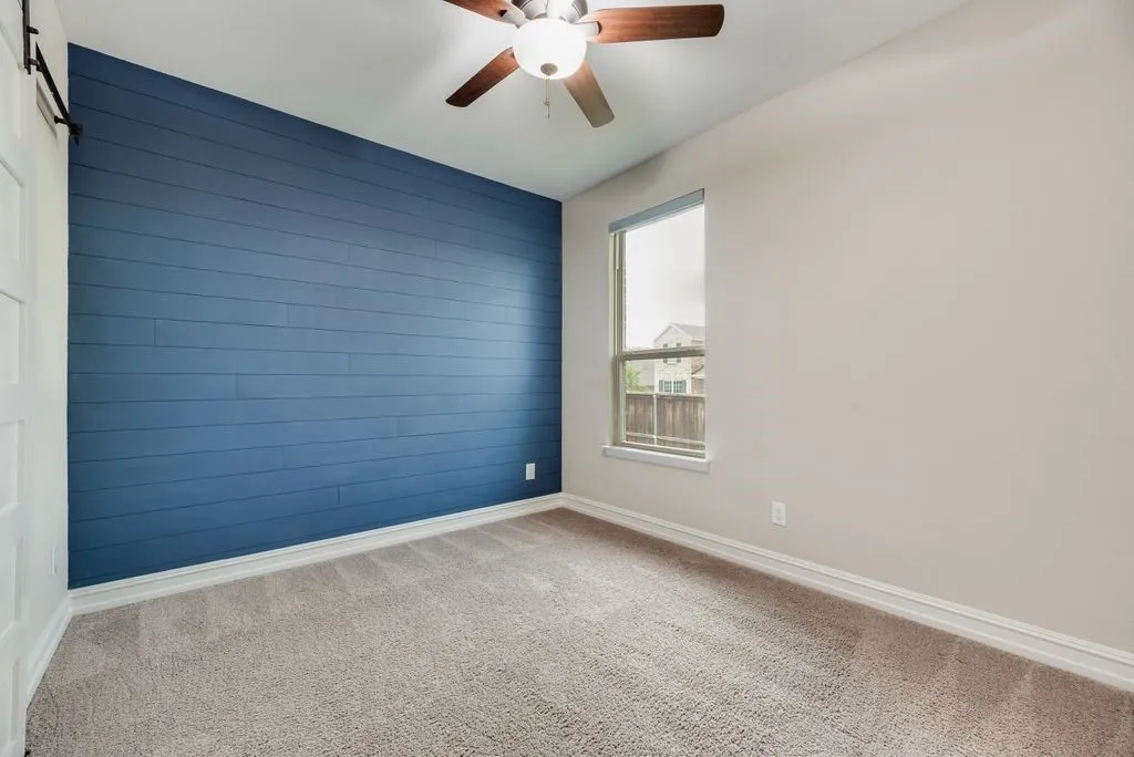 Bedroom 3 - Plank accent wall, carpet flooring, ceiling fan with light fixture, single window, and white trim
