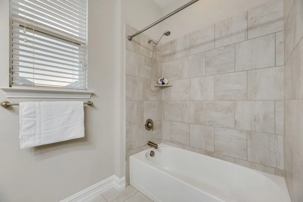 Bathroom 2 - White bathtub with an integrated shower, surrounded by rectangular tile walls, featuring a built-in shelf and brushed nickel fixtures