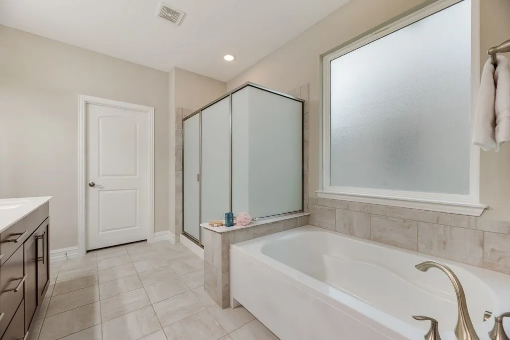 Soaking tub with brushed nickel fixtures, a framed glass shower enclosure, and a frosted privacy window
