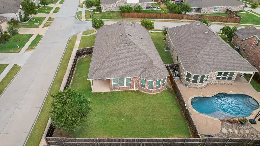 Aerial view showcasing a spacious residential lot with manicured lawn, mature landscaping, and brick exterior