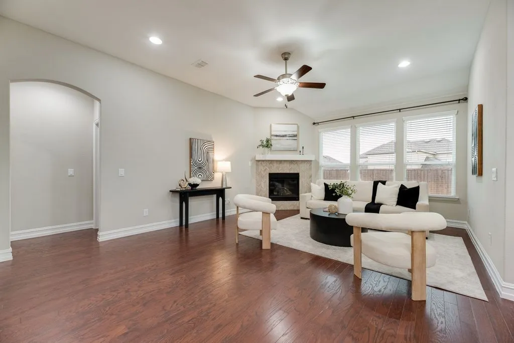 Vaulted ceiling with a ceiling fan, fireplace with a tile surround, multiple windows with blinds, recessed lighting, and wood-finish flooring