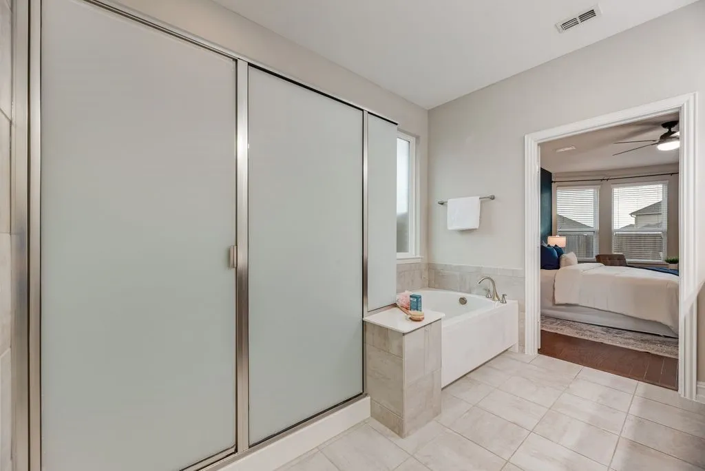 Frosted glass shower enclosure, built-in soaking tub, tiled flooring, and light neutral wall finishes