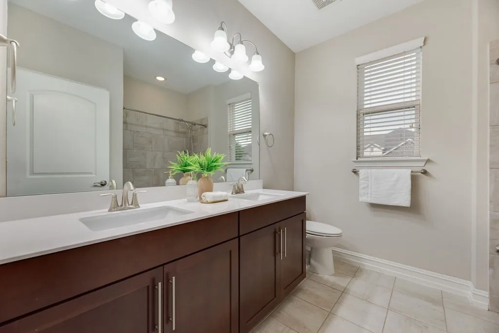 Bathroom 2 - Dual vanity with white undermount sinks and brushed nickel faucets, dark wood-finish cabinetry, white countertop, large mirror, and tiled flooring