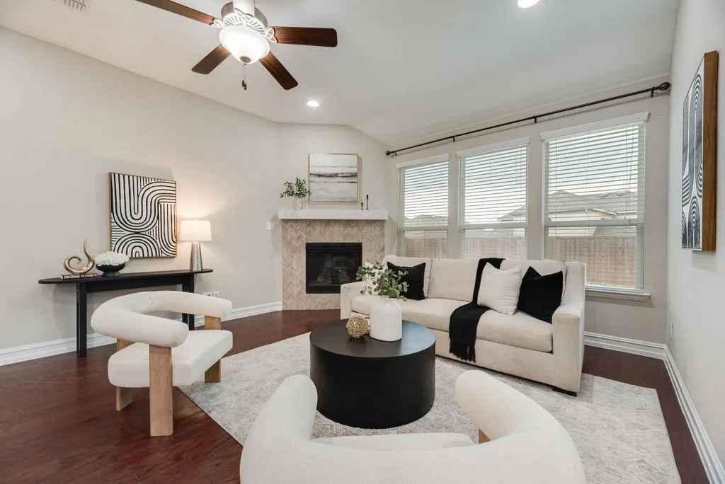 Hardwood-style flooring, a corner fireplace with herringbone tile surround, a ceiling fan, recessed lighting, and multiple windows with blinds