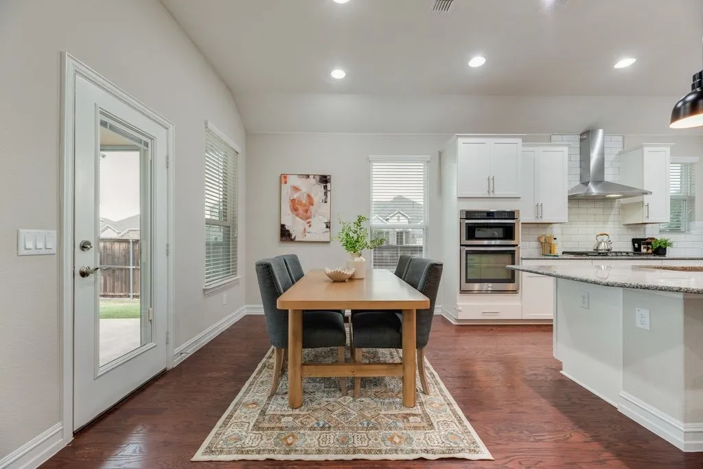 Kitchen and dining area featuring wood-finish flooring, white cabinetry, stainless steel appliances, and an external glass panel door