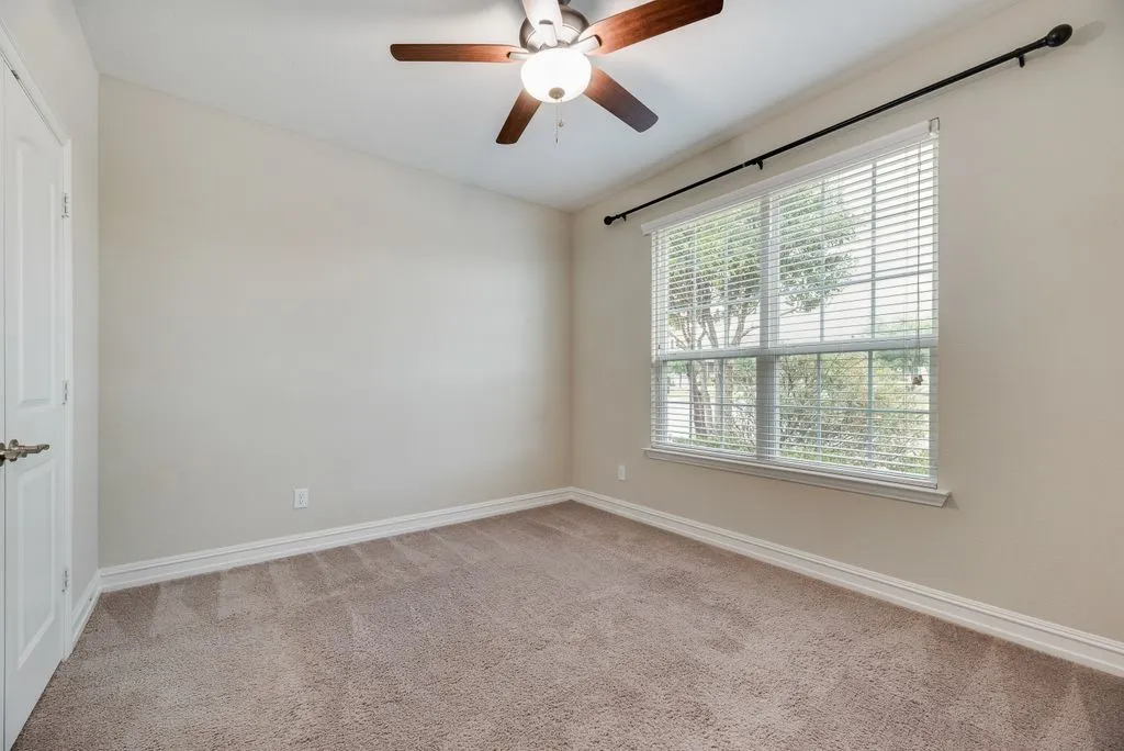 Bedroom 2 - Neutral-toned carpeting, ceiling fan with light fixture, window with blinds, and a white paneled door.