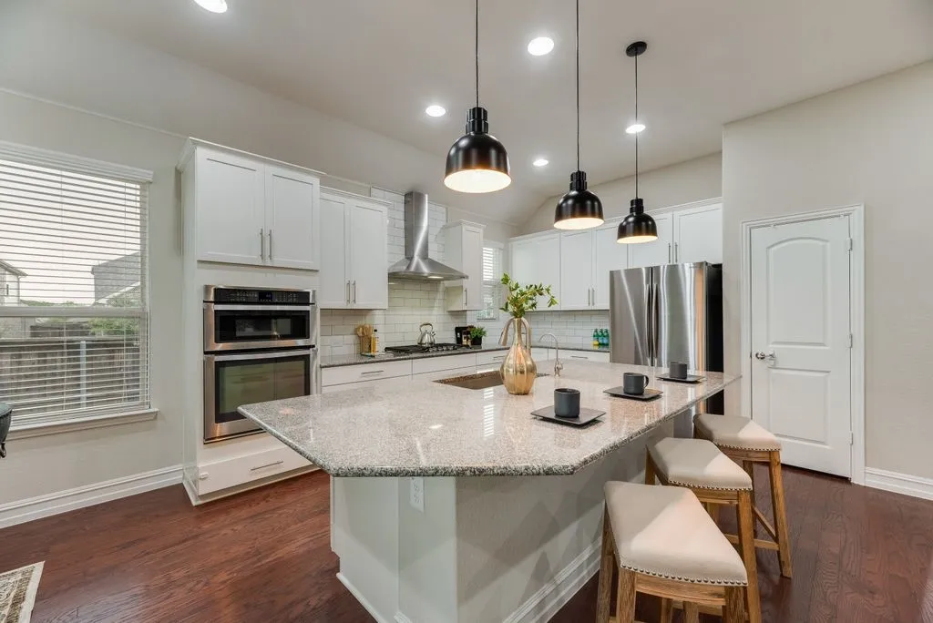 Kitchen featuring wood-finish flooring, a multi-level island with seating, stainless steel appliances, white cabinetry, and recessed lighting