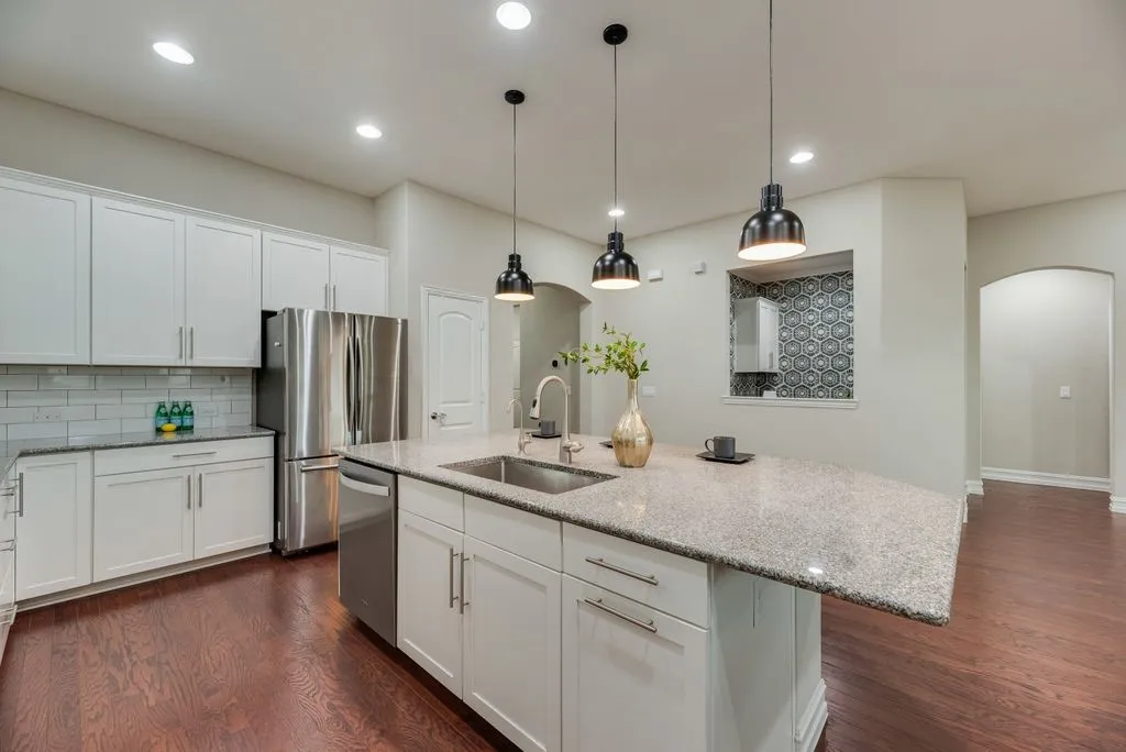 White shaker-style cabinetry, stainless steel appliances, wood-finish flooring, island with integrated sink, and recessed lighting