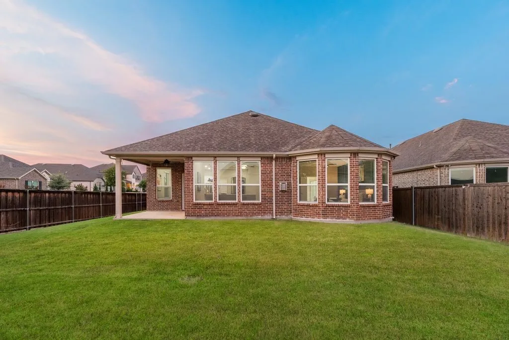 Expansive backyard featuring a manicured lawn, full privacy fencing, a covered patio, and a brick exterior with multiple large windows