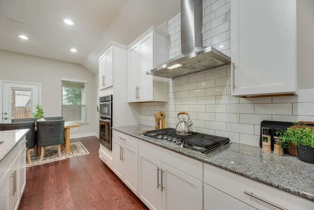 Kitchen featuring white cabinetry, a 5 burner gas cooktop, stainless steel wall-mounted oven and microwave, light-toned stone countertops, and wood-finish flooring