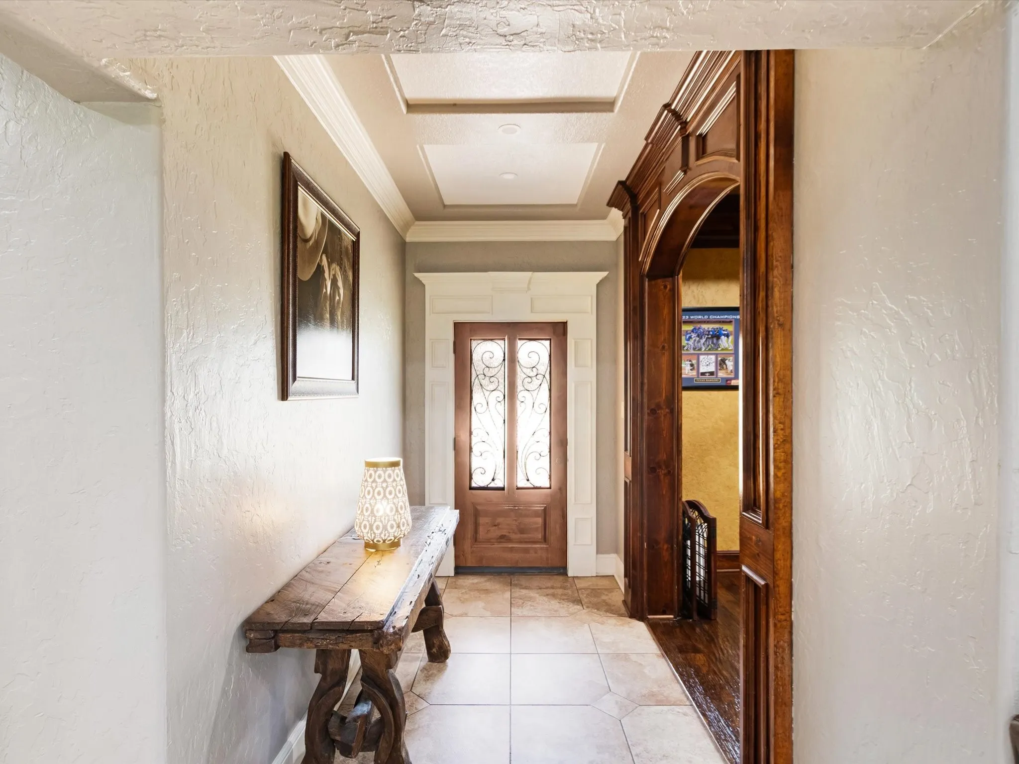 Hallway featuring coffered ceiling detail, wood-finish entry door with decorative glass, tile flooring, and a decorative wood archway