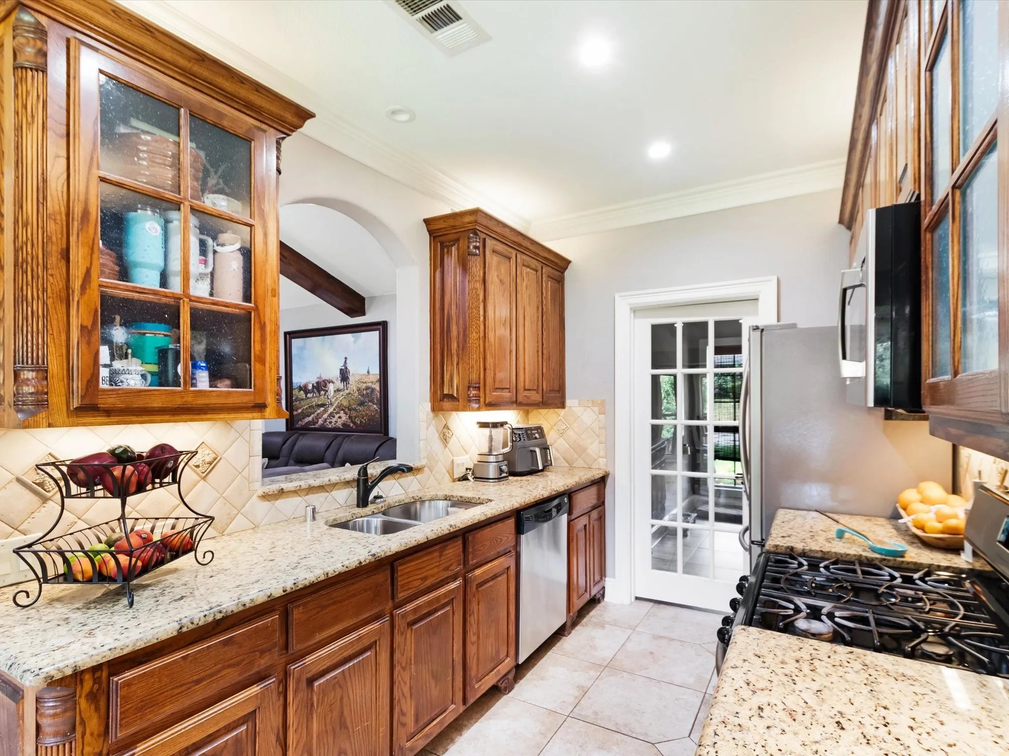 Wood-finish cabinetry with glass-front uppers, granite countertops, tile backsplash, and stainless steel appliances